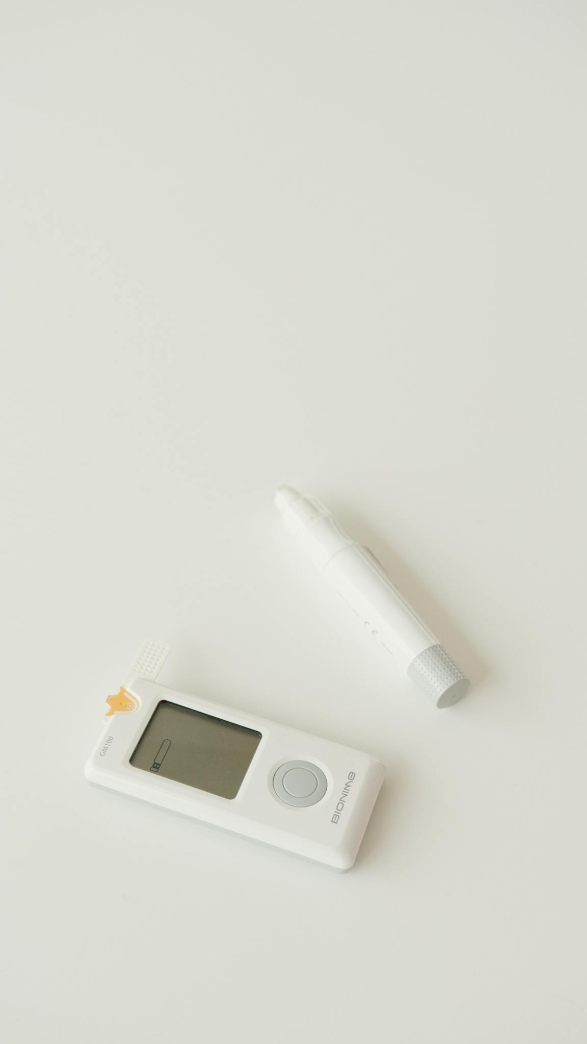 A digital glucometer and pen set against a minimalist white backdrop, symbolizing health monitoring.